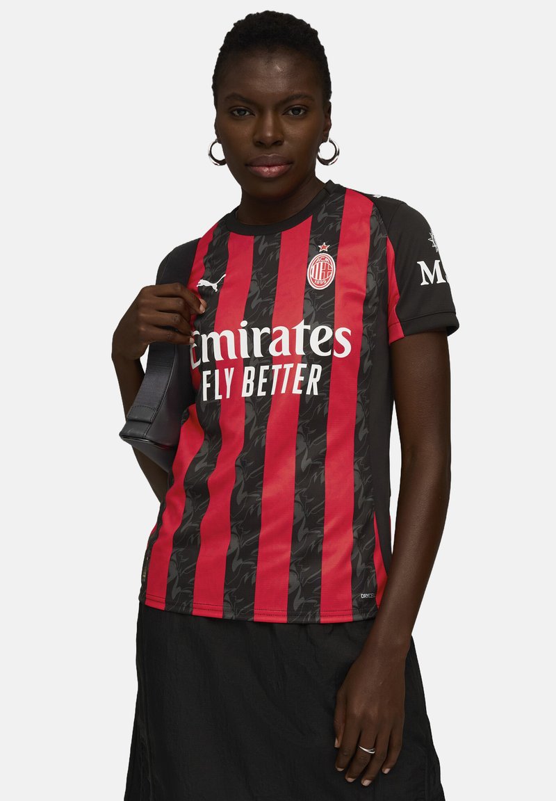 Maillot de football à manches courtes noir et rouge à rayures, avec un motif texturé, un logo blanc et le texte "Emirates Fly Better" à l'avant.