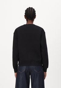 Sudadera de algodón negra con cuello redondo, manga larga y corte relajado. La parte de atrás presenta costuras suaves y un diseño minimalista.