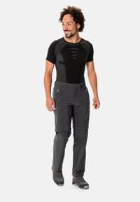 Zwart aansluitend shirt met korte mouwen en textuurpanelen, gecombineerd met grijze convertible broek. De broek heeft ritszakken en verstelbare manchetten.