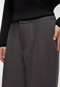 Pantaloni grigi su misura realizzati in un tessuto liscio e leggero. Presentano una vita piatta con sottili pince e tasche laterali.