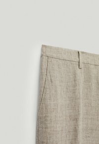 Pantalon en lin beige avec un tissage texturé, doté de poches latérales et d'une taille plate à l'avant, illustrant une coupe décontractée.