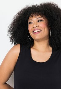 Svart ärmlös linne med rundad halsringning, tillverkat av ett mjukt tyg. Har en avslappnad passform och synliga sömmar längs kanterna.