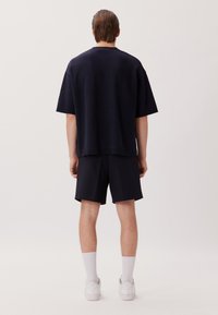 T-shirt sovradimensionato blu navy con texture e scollatura rotonda, abbinato a pantaloni corti neri. Calzini bianchi e sneakers completano l'outfit.