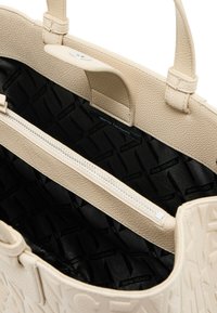 Sac à main beige avec un extérieur en cuir texturé, doté de courtes anses et d'un intérieur noir à motifs, comprenant une poche zippée.