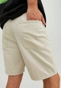 Pantaloni corti in cotone beige con taglio dritto, due tasche posteriori, cuciture a vista e una consistenza morbida. Indossati con una camicia nera.