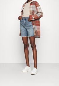 Rutig flanellskjorta i röd och beige, ihopparad med blå denimshorts med fransad nederkant, och vita sneakers. Enkel och avslappnad look.