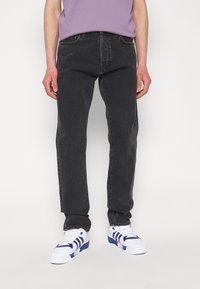 Sorte denimbukser med rett passform, som har fem lommer og subtile falminger. Brukt med hvite sneakers og en lilafarget t-skjorte.