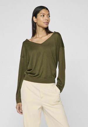 Suéter liviano de punto color verde oliva con escote en V, hombros caídos y un ajuste relajado, combinado con pantalones de color crema.