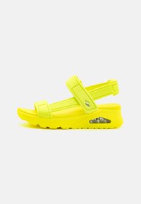 Sandali giallo brillante con suola imbottita, cinturini regolabili e una bolla d'aria visibile sul lato per comfort e supporto.