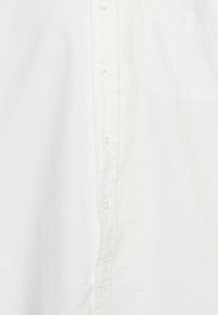 Vit skjorta med knappar i bomull med en slät yta. Har en framknäppning, klassisk krage och en bröstficka.