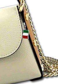 Beige leren handtas met een gouden kettingstrap, voorzien van een klein Italiaans vlaggetje als bedel aan de zijkant en een gladde, glanzende afwerking.