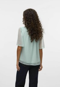 Ljus mintgrön blus med genomskinliga, korta puffärmar och prickigt mönster. Baksidan är något längre med en mjuk textur.