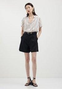 Blusa a maniche corte a righe in crema e nero abbinata a pantaloni corti neri a vita alta. Una cintura nera e sandali neri con cinturini completano il look.