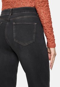 Jean en denim noir avec une taille haute, comportant deux poches arrière et des coutures visibles. Les jeans ont une texture lisse et une coupe ajustée.