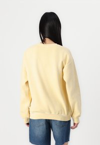 Gul sweatshirt med avslappnad passform, rund halsringning, ribbade ärmslut och nederkant, tillverkad av mjukt material. Bärs med denimshorts.