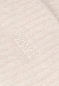 Tissu beige clair et duveteux avec une texture douce, arborant une étiquette blanche portant la mention "10DAYS". Le design présente de fines rayures verticales.