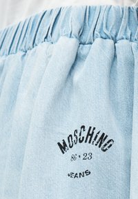 Ανοιχτό μπλε ύφασμα τζιν με ραμμένη ελαστική μέση και μαύρο λογότυπο Moschino Jeans 86•23 τυπωμένο στο υλικό.