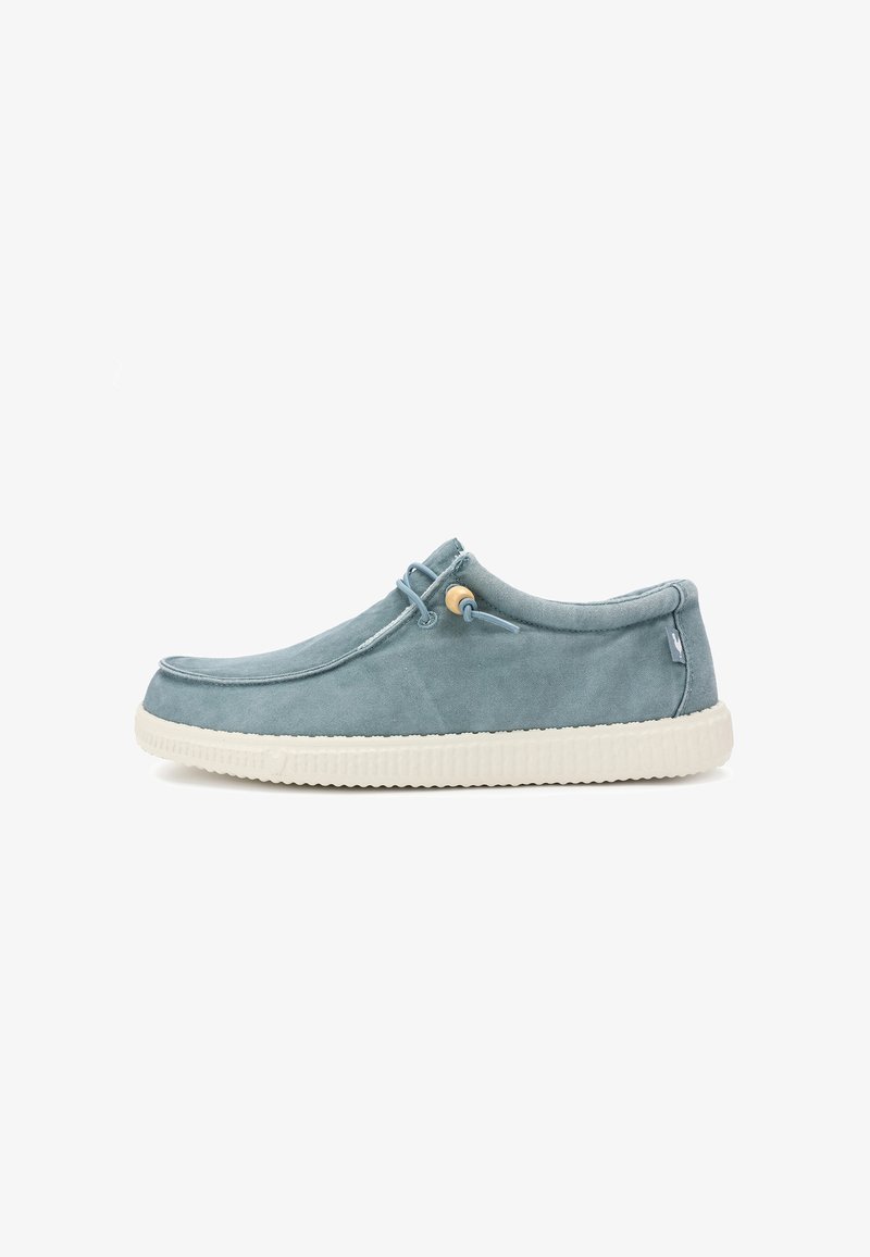 Chaussure décontractée slip-on en suède bleu clair avec semelle en caoutchouc blanche et lacet latéral avec détail de perle en bois, vue de profil sur fond blanc.