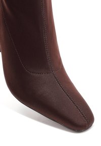 Bottine marron à bout pointu, texture lisse et détail de couture diagonale. Fabriquée en matériau doux avec un design ajusté.