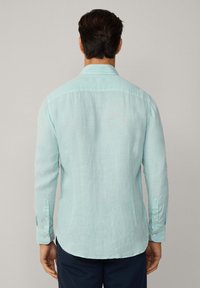 Camisa de manga larga azul claro hecha de lino, con un cuello clásico, puños abotonados y un dobladillo curvado. Diseño de tela simple y texturizada.