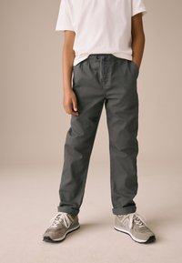 Pantalon gris à taille élastique avec cordon de serrage, doté de poches latérales et d'une coupe décontractée, associé à des baskets grises avec des accents blancs.