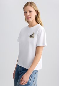 Hvid bomulds T-shirt med en afslappet pasform, der har et dekorativt båddesign i sort og sølv rhinsten på venstre brystområde.