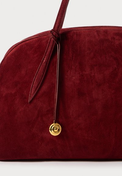 Borsa a mano rossa in suede, con una forma arrotondata, caratterizzata da un dettaglio in metallo dorato a forma circolare e una tracolla coordinata. Texture morbida e design minimalista.