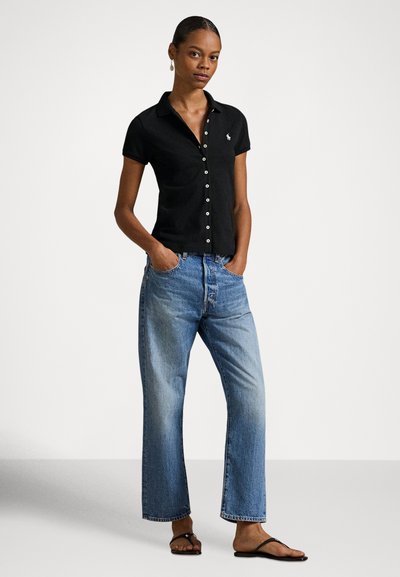 Czarna polo z krótkim rękawem, kołnierzykiem i pliską na guziki, w połączeniu z jasnoniebieskimi dżinsami o szerokich nogawkach i czarnymi klapkami.