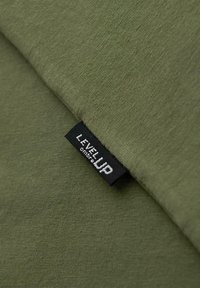 Tissu vert avec une étiquette tissée noire cousue, affichant le texte blanc "LEVEL UP" et un texte plus petit en dessous.