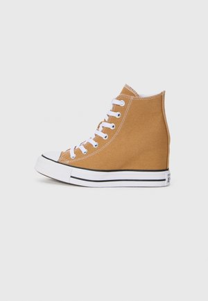 Klasické vysoké tenisky z hnědé plátna s bílými tkaničkami, gumeným prstovým chráničem a černě pruhovanou podrážkou. Texturovaný povrch se švy.