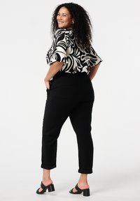 Pantalons noirs fuselés avec des revers et des poches latérales, associés à un chemisier à motifs abstraits noir et blanc. Portés avec des sandales à talons noires.