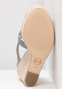 Niebieskie sandały na koturnie z denimu z plecionym wykończeniem z juty, gumową podeszwą i wytłoczonym logo na wewnętrznej stronie. Posiadają krzyżujące się paski dla wsparcia.