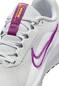 Sneaker Nike en mesh blanc avec des accents violets. Présente une tige texturée, un design swoosh proéminent et une languette rembourrée avec une sangle violette.
