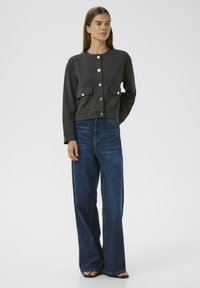 Šedá dlouhá cropped bunda s kulatým výstřihem, zlatými knoflíky, předními kapsami, spárovaná s modrými džínami s vysokým pasem a širokými nohavicemi.