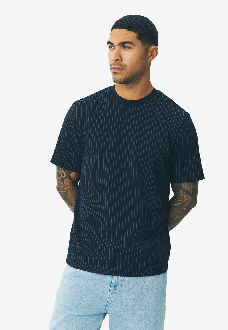 Sort T-shirt med tynde lodrette hvide striber, lavet af bomuldsblanding, med rund halsudskæring og korte ærmer, parret med lyseblå jeans.