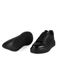 Schwarze Sneakers mit einem glatten Lederobermaterial und strukturierten Wildlederakzenten. Merkmale eine dicke Gummisohle mit geometrischem Profil und runden Schnürsenkeln.