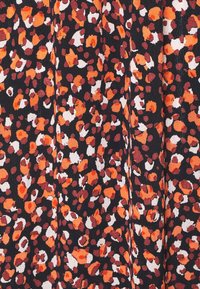 Tissu noir avec un motif floral abstrait en taches orange, blanches et brunes, montrant une texture et de légères ondulations.