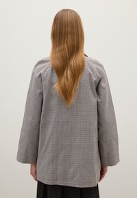 Houndstooth-patroon langarmshirt in zwart en wit, met een relaxte pasvorm en een rechte zoom. De achterkant toont ruime mouwwijdte.