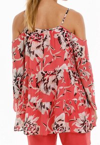 Top floral corail avec un design à épaules dénudées, des volants et de fines bretelles. Présente de grands motifs floraux roses et noirs.