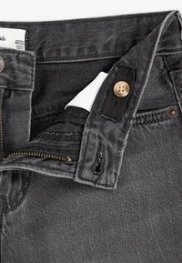 Jeans de mezclilla gris oscuro con cremallera, cierre de botón y detalles de tela negra. Presenta una cinturilla con costuras y una etiqueta de algodón en el interior.