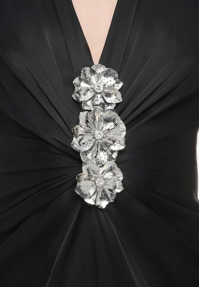 Fekete ruha mély V-nyakkivágással, középen három fémes virágapplikációval, a teljes felületen redős textúrával.