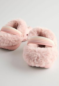 Chaussons pelucheux rose clair avec une épaisse doublure en fausse fourrure et des semelles en caoutchouc ; présentent une large sangle douce d'une teinte de rose légèrement plus foncée.