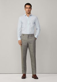 Camicia button-up azzurro chiaro con maniche lunghe, abbinata a pantaloni grigi chiari su misura. Scarpe in pelle marrone completano l'outfit.