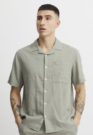 Chemise vert clair à manches courtes en tissu texturé, dotée d'une fermeture à boutons sur le devant, d'une poche poitrine unique et d'un col décontracté.