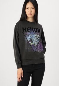 Felpa grigio scuro con una grafica triangolare raffigurante un leone che ruggisce in viola e blu, e la parola "HÉROÏC" stampata in grassetto nero.