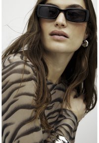 Black rectangular sunglasses, sheer top with zebra print, silver jewelry accents, long brown hair, neutral makeup, soft texture, close-up view.