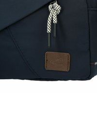 Mørkeblå stof skuldertaske med en tekstureret læderdetalje, der har en snorelukning og en kontrasterende hvid og sort snor.