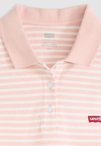 Polo shirt a righe rosa e bianche con colletto, tre bottoni e un logo rosso Levi's sul lato sinistro del petto. Materiale in cotone, finitura testurizzata.