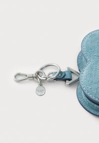 Sininen farkkukotelo hopeisella hardwarella, avaimenperäkiinnikkeellä ja Kate Spade -tunnuksella. Pyöreä muotoilu, jossa on teksturoitu kangas ja kontrastiväriset ompeleet.