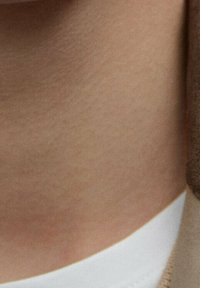 Beige stof met een gladde textuur toont een close-up van huid en een witte rand, mogelijk van een kledingstuk of accessoire, in zacht natuurlijk licht.